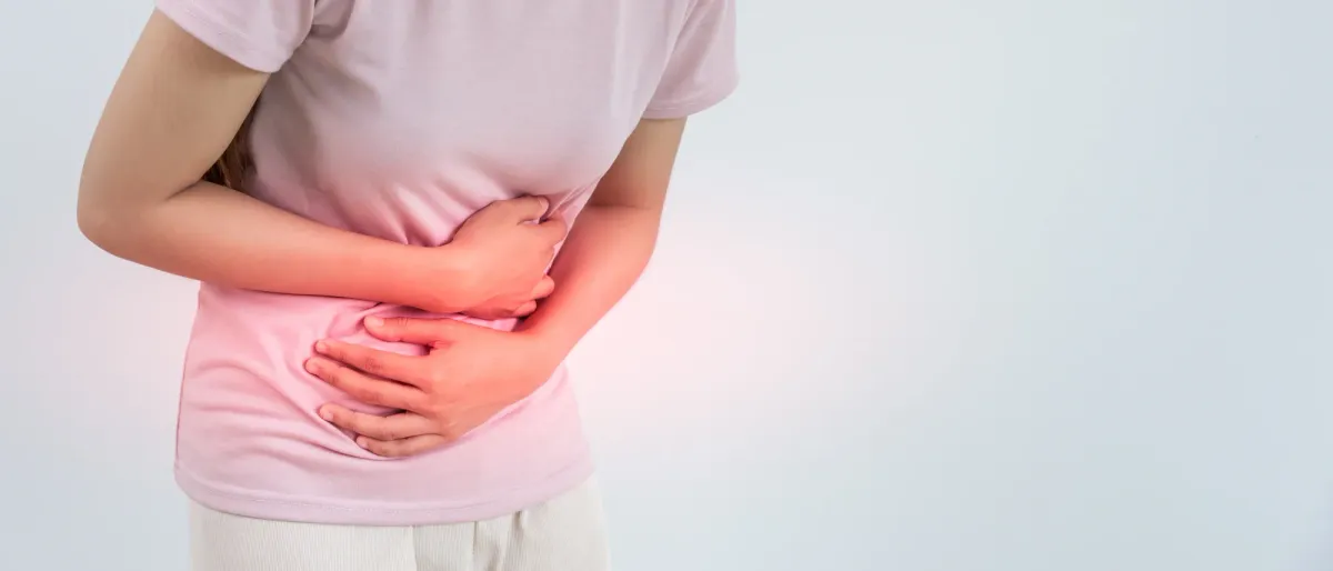 Femme en tee-shirt, les mains repliées sur le bas-ventre douloureux