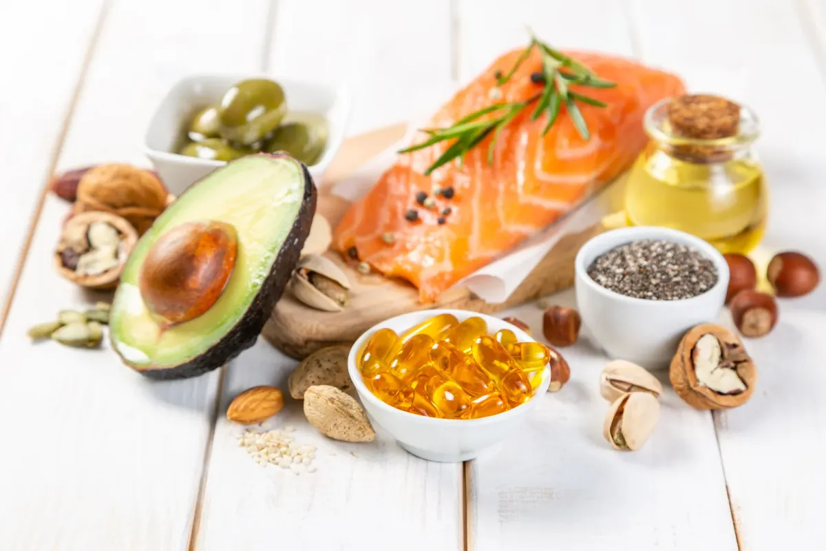 Saumon, avocat, noix, graines de chia et huile d'olive posés sur une planche claire