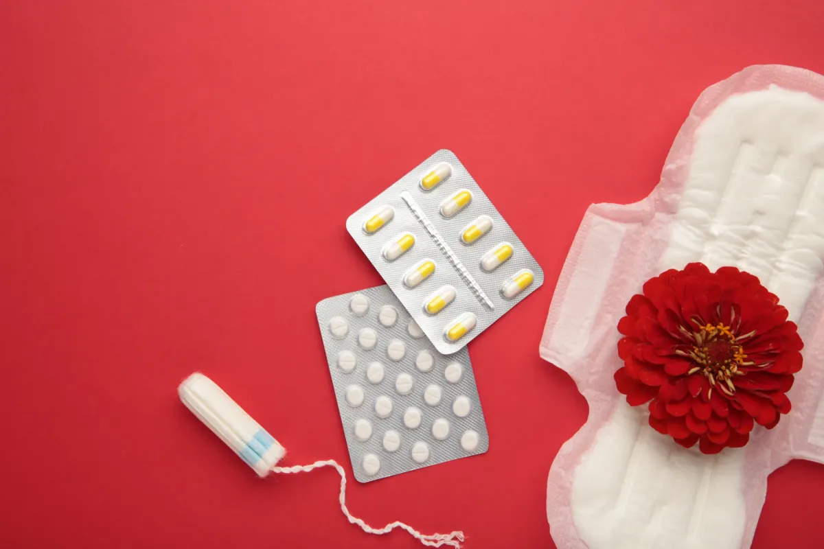 Antalgiques, tampon et serviette hygiénique posés sur un fond rouge