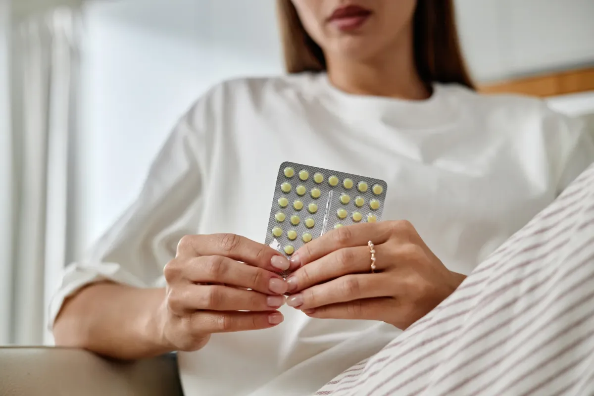 Femme tenant sa plaquette de traitement hormonal, assise dans son salon