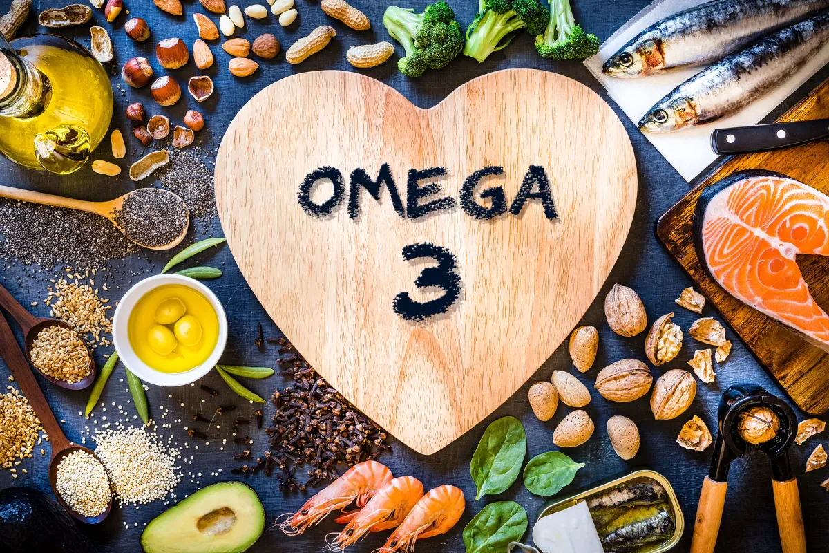 Aliments riches en oméga-3 autour d'une planche en forme de cœur : poissons gras, noix, graines, avocat