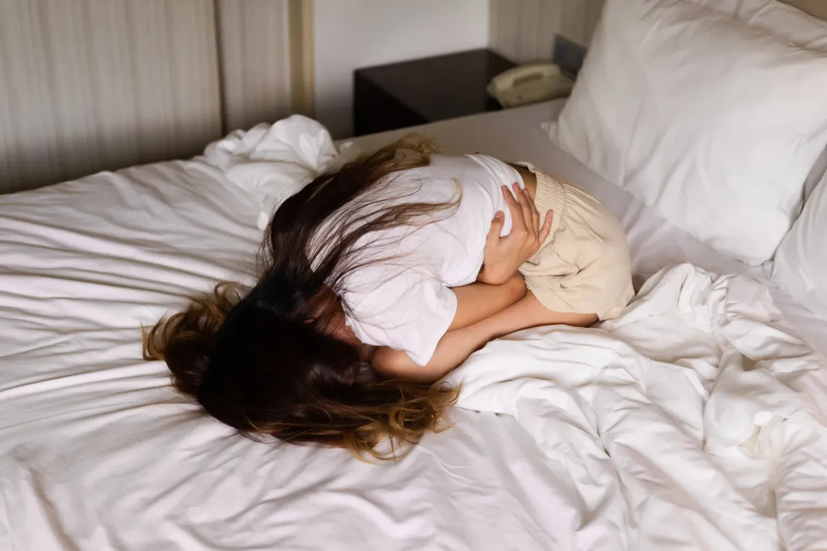 Femme recroquevillée dans son lit au petit matin, réveillée par la douleur