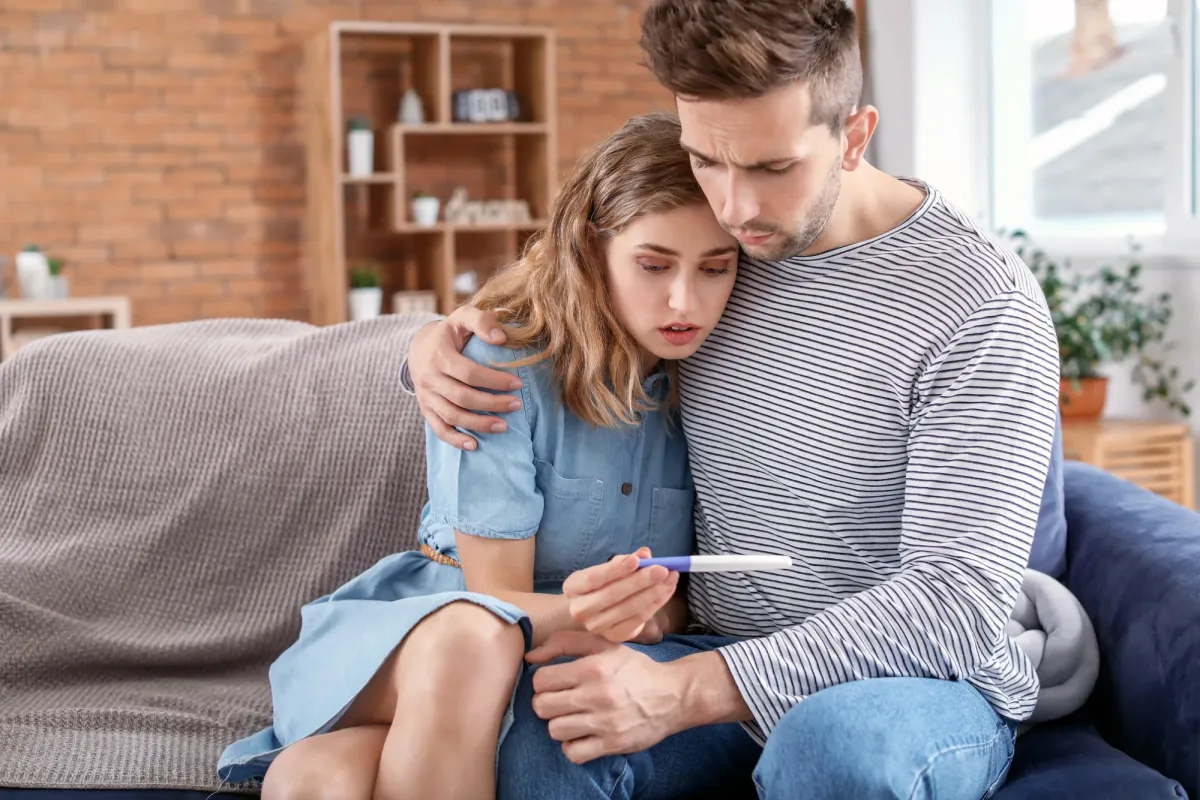 Couple assis sur un canapé, regardant ensemble un test de grossesse