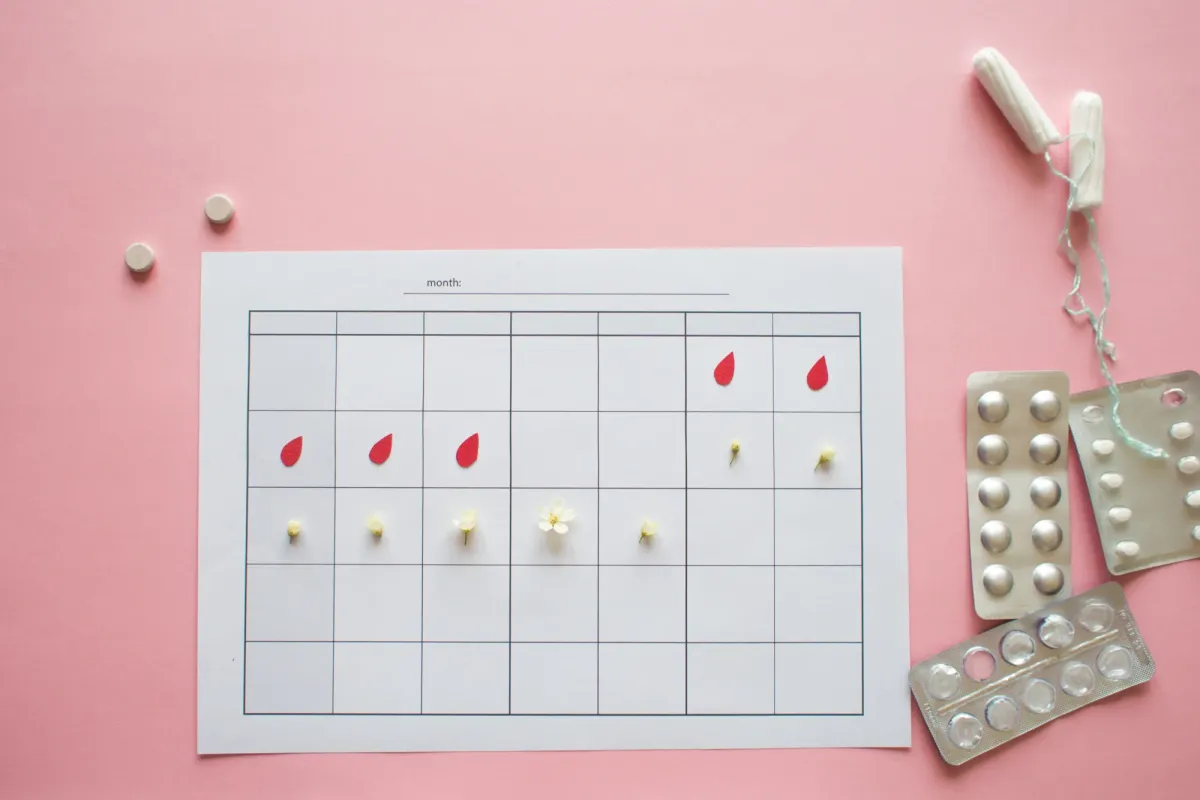 Calendrier mensuel de suivi des règles posé à côté de plaquettes de traitement hormonal