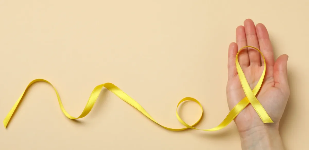 Ruban jaune de sensibilisation à l'endométriose posé dans une main ouverte, sur fond beige
