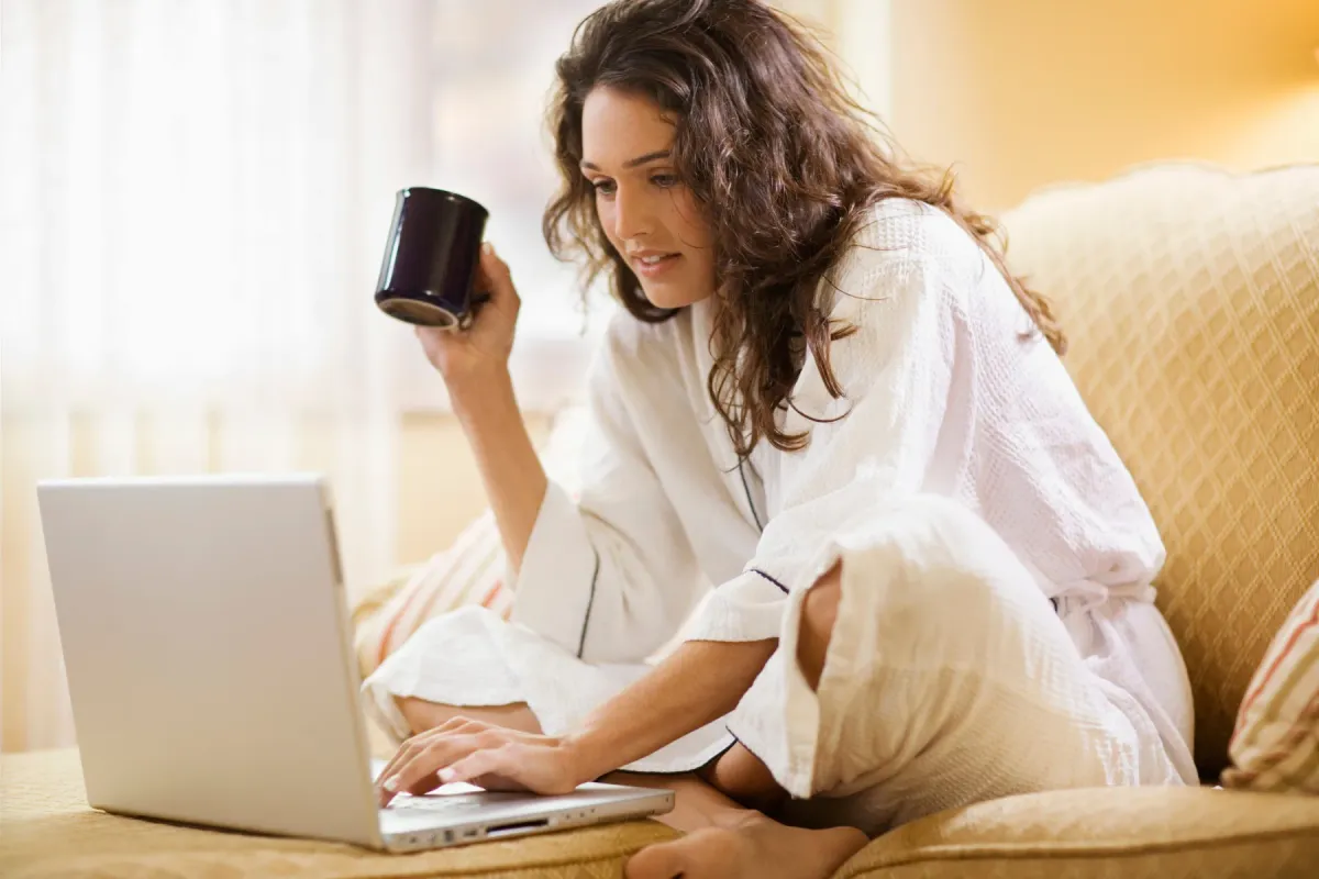 Femme travaillant chez elle avec son ordinateur portable, une tasse à la main