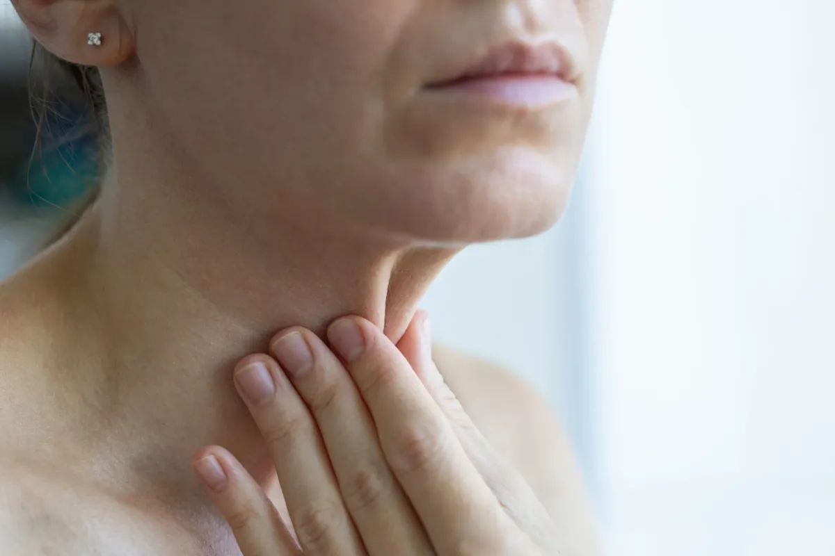 Femme posant doucement la main sur son cou, à hauteur de la thyroïde