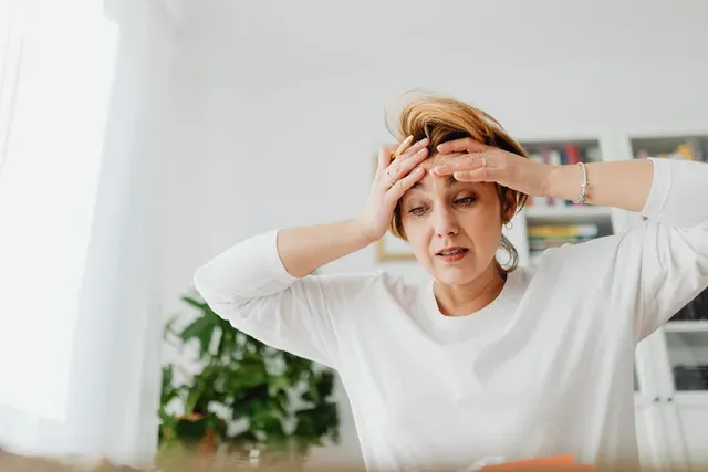 Femme les deux mains sur le front, le visage crispé par un mal de tête