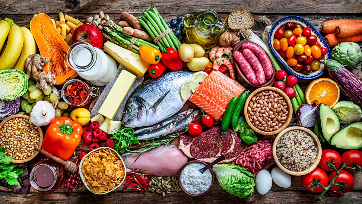 Grande variété d'aliments anti-inflammatoires sur un plan de travail en bois : poissons gras, sardines, noix, graines, légumes verts, gingembre, avocat