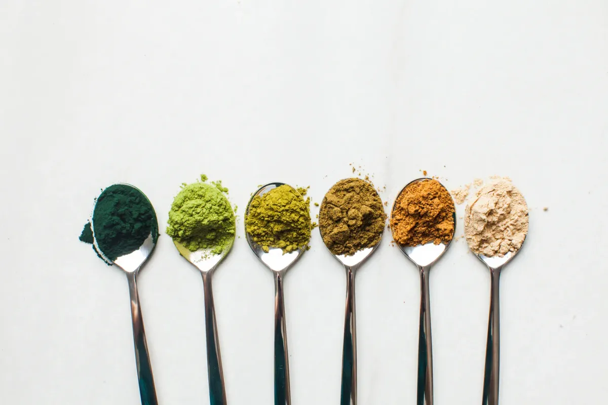 Cuillères de poudres de super-aliments alignées : spiruline, matcha, curcuma, maca