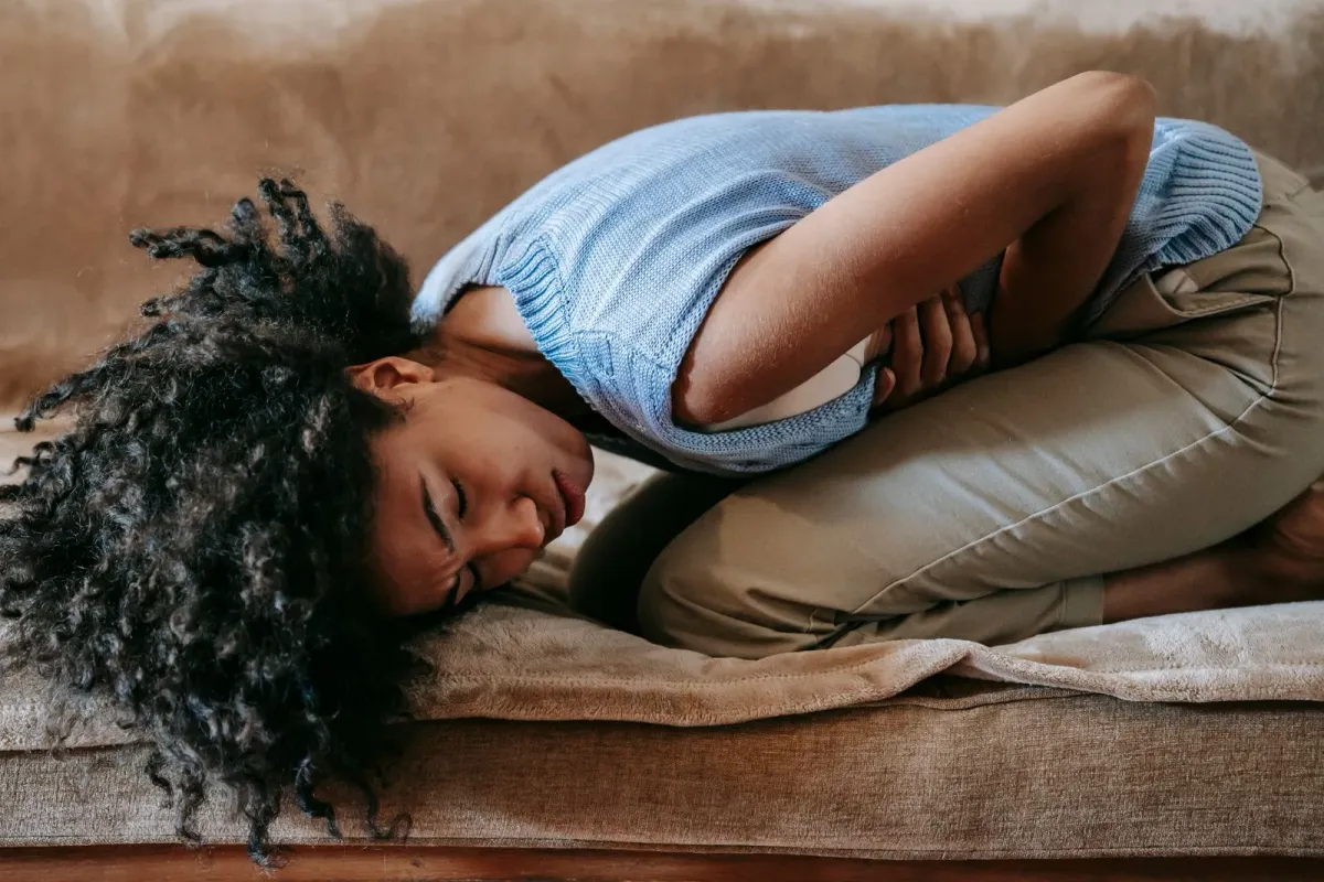Femme allongée sur un canapé, repliée sur elle-même, les mains sur le bas-ventre