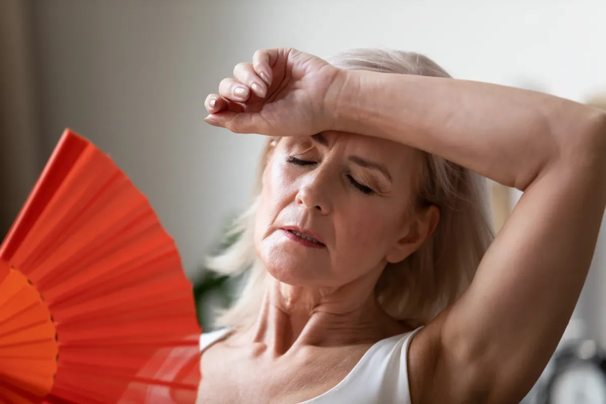 Femme aux cheveux clairs s'éventant avec un éventail rouge, la main sur le front