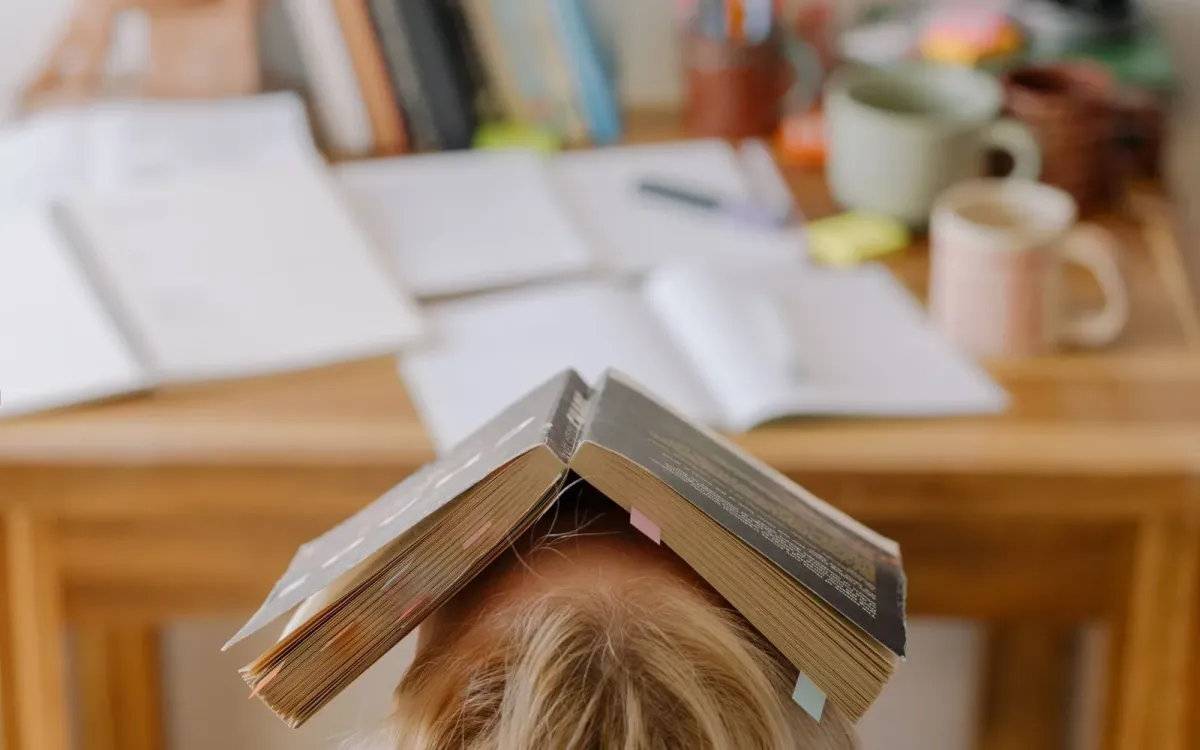 Femme assise à sa table, un livre ouvert posé sur la tête