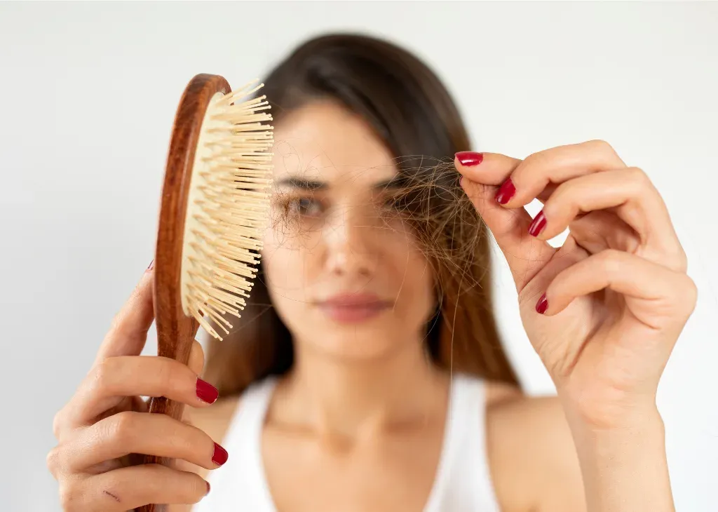 Femme brune tenant une brosse en bois et une mèche de cheveux tombés