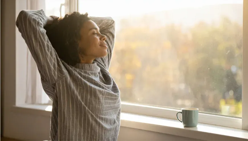 Femme qui s'étire devant une fenêtre baignée de lumière du matin