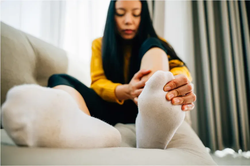 Femme assise sur un canapé qui tient son pied et son mollet