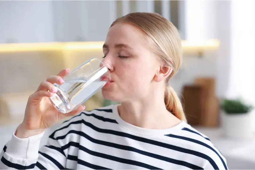 Femme en pull rayé buvant un verre d'eau dans une cuisine lumineuse