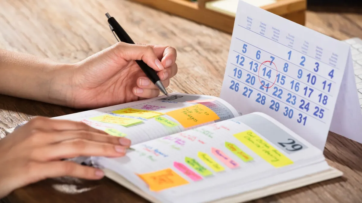 Mains annotant un agenda à côté d'un calendrier, une date entourée en rouge