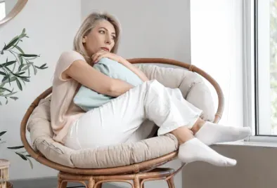 Femme repliée sur elle-même dans un fauteuil rond, près d'une fenêtre