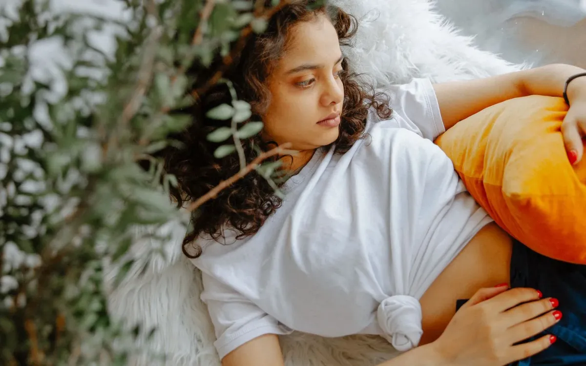 Jeune femme allongée sur un plaid, un coussin serré contre le ventre, près de plantes vertes