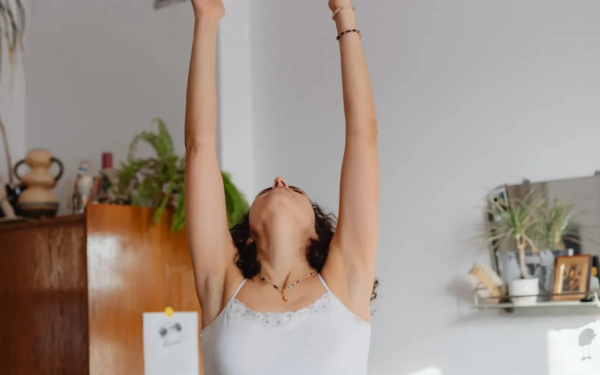 Femme debout chez elle, bras levés au-dessus de la tête dans un étirement, lumière du matin Femme debout chez elle, bras levés au-dessus de la tête dans un étirement, lumière du matin
