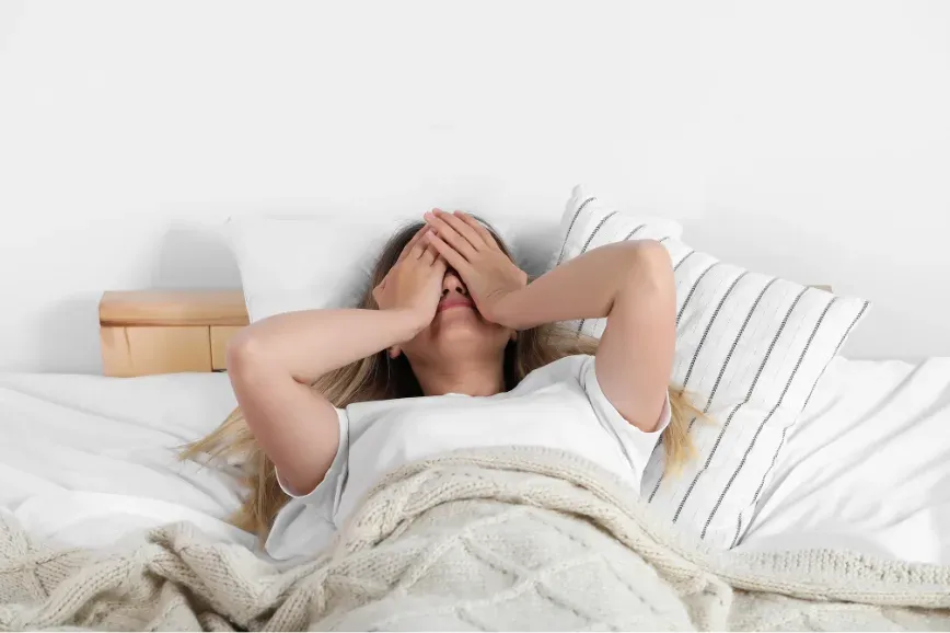Femme allongée dans son lit au réveil, les mains sur le visage