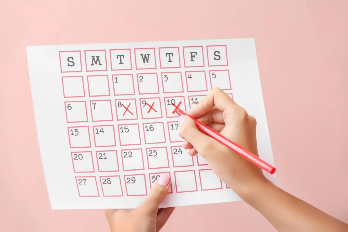 Main notant les dates de ses règles sur un calendrier papier