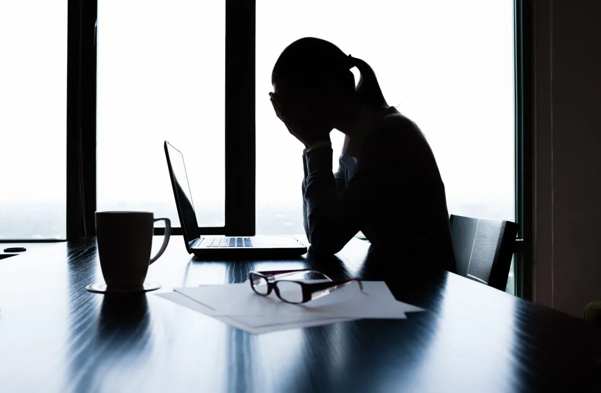 Femme assise à son bureau dans la pénombre, la tête dans les mains devant son écran