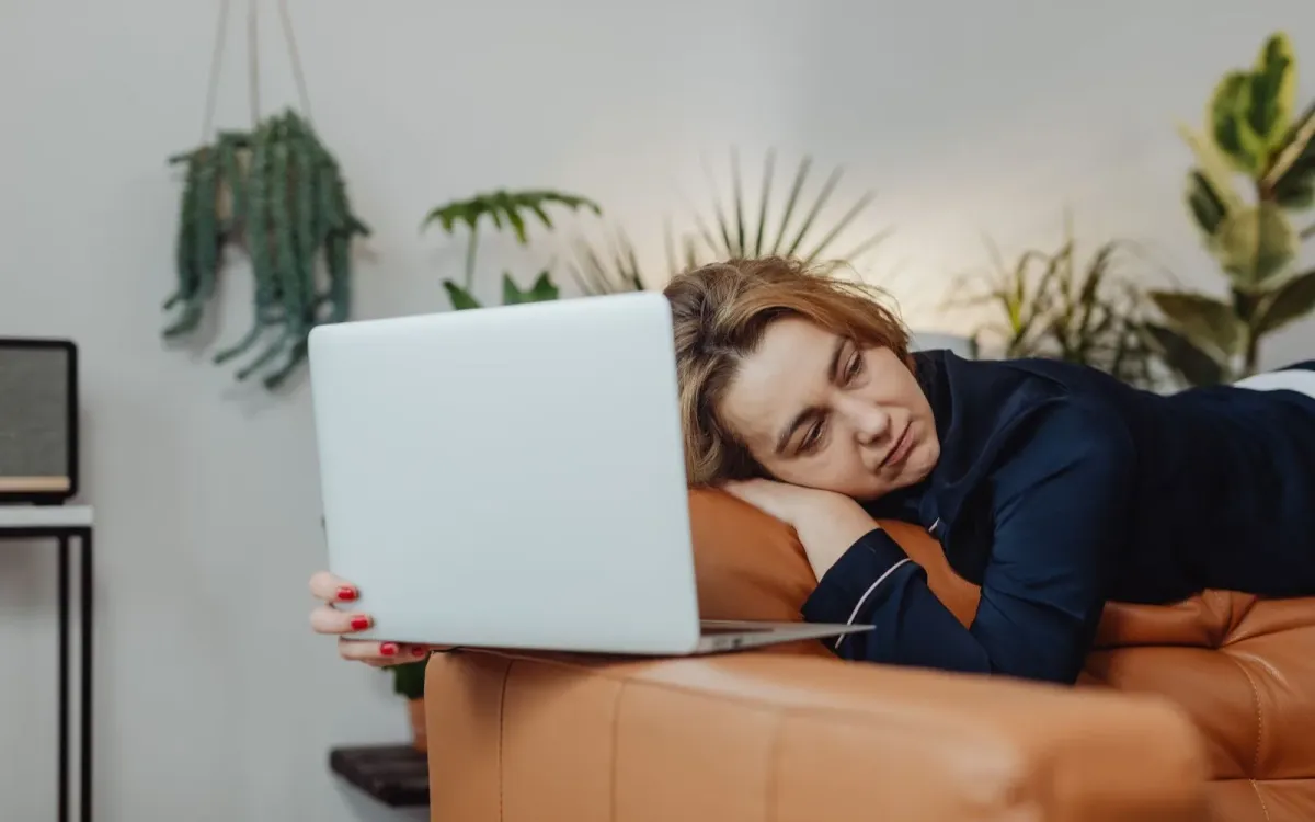 Femme assoupie sur son canapé, l'ordinateur portable encore ouvert à côté d'elle