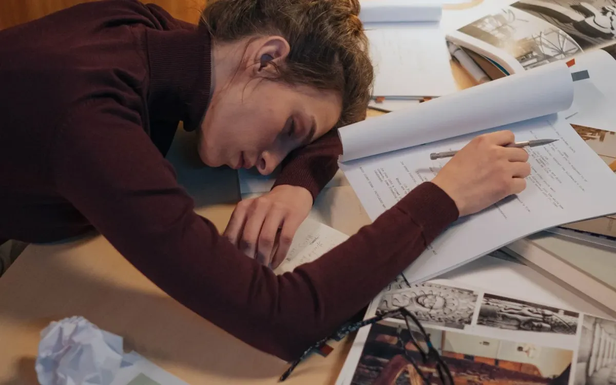 Femme épuisée s'endormant à son bureau, la tête posée sur son avant-bras
