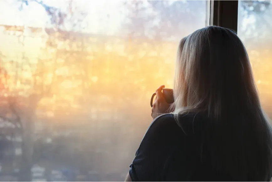 Femme devant une fenêtre au lever du jour, la lumière dorée sur le visage