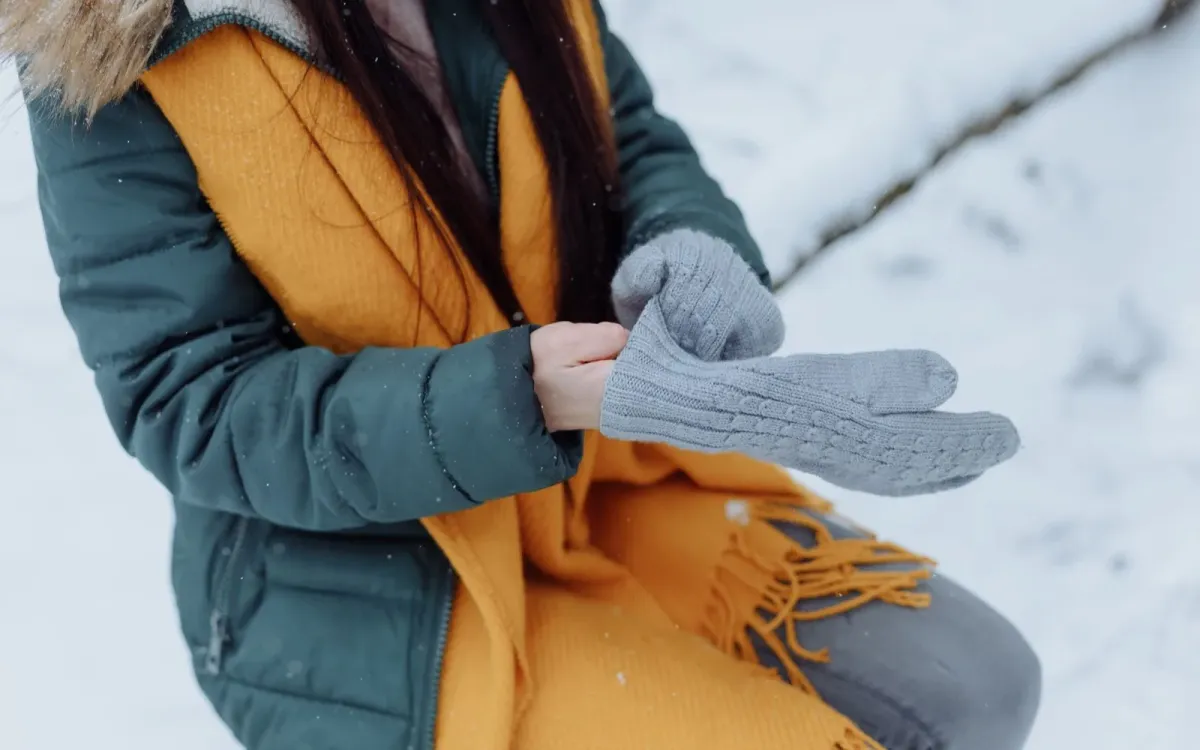Femme en manteau d'hiver ajustant ses gants gris sous la neige Femme en manteau d'hiver ajustant ses gants gris sous la neige