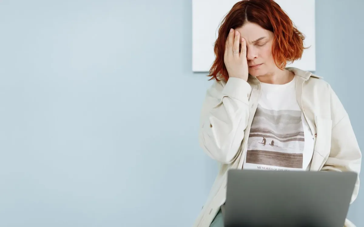 Femme assise devant son ordinateur, tendue, la main sur le front