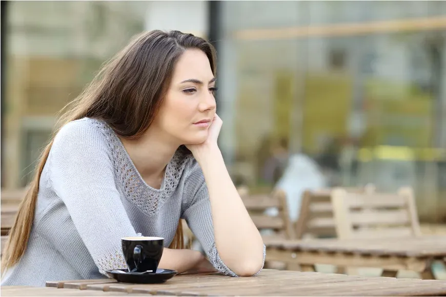 Femme pensive attablée en terrasse, le menton posé sur la main