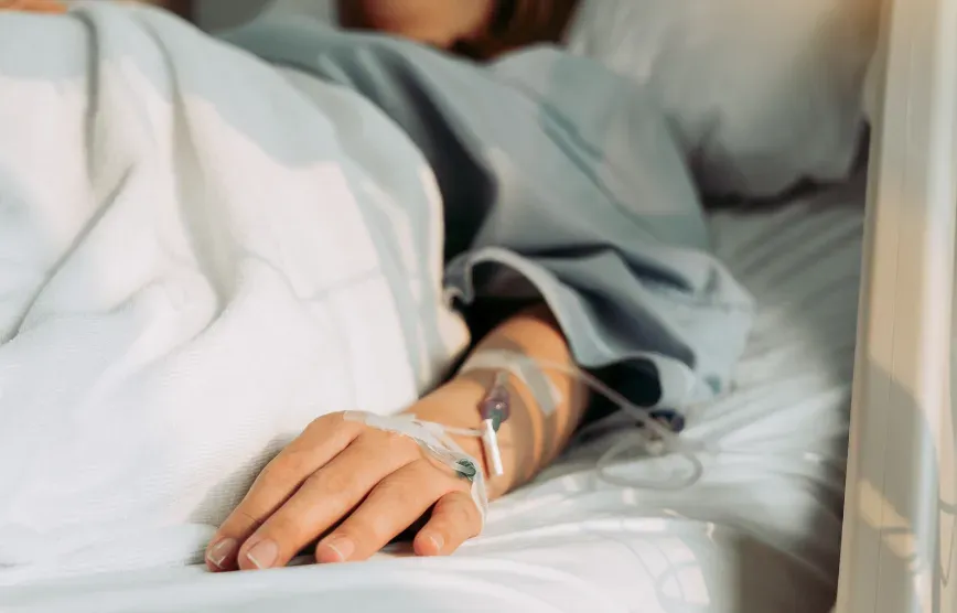 Main d'une patiente allongée dans un lit d'hôpital, perfusion posée sur le dos de la main
