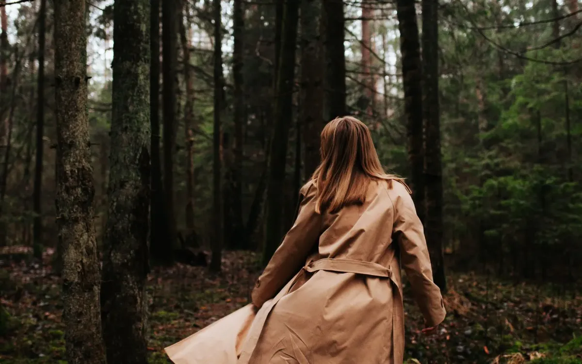 Femme en trench sur un chemin de forêt