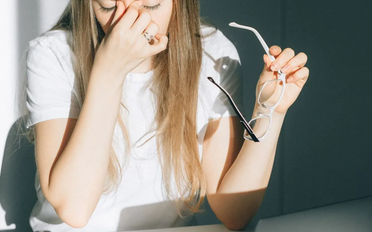 Jeune femme retirant ses lunettes, les yeux fermés, gênée par la lumière