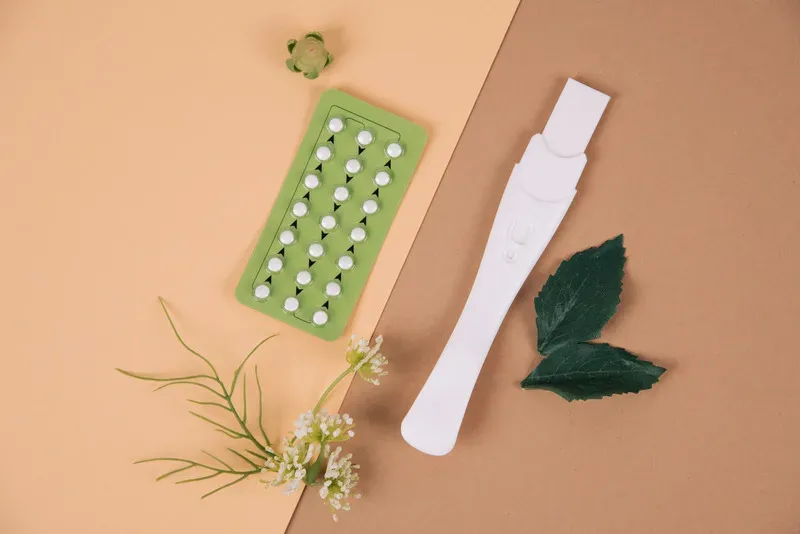 Plaquette de contraception, test et brins de plantes posés sur fond beige