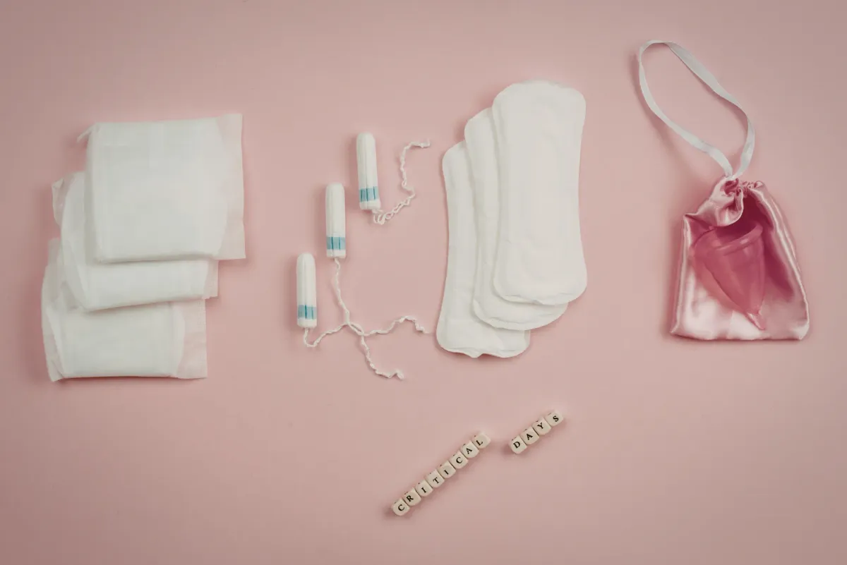 Serviettes, tampons, protège-slips et coupe menstruelle disposés à plat sur fond rose, en lien avec les règles abondantes