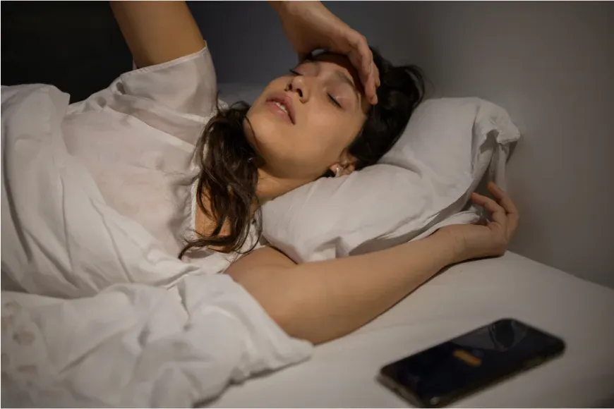 Femme réveillée en pleine nuit dans son lit, téléphone posé à côté d'elle