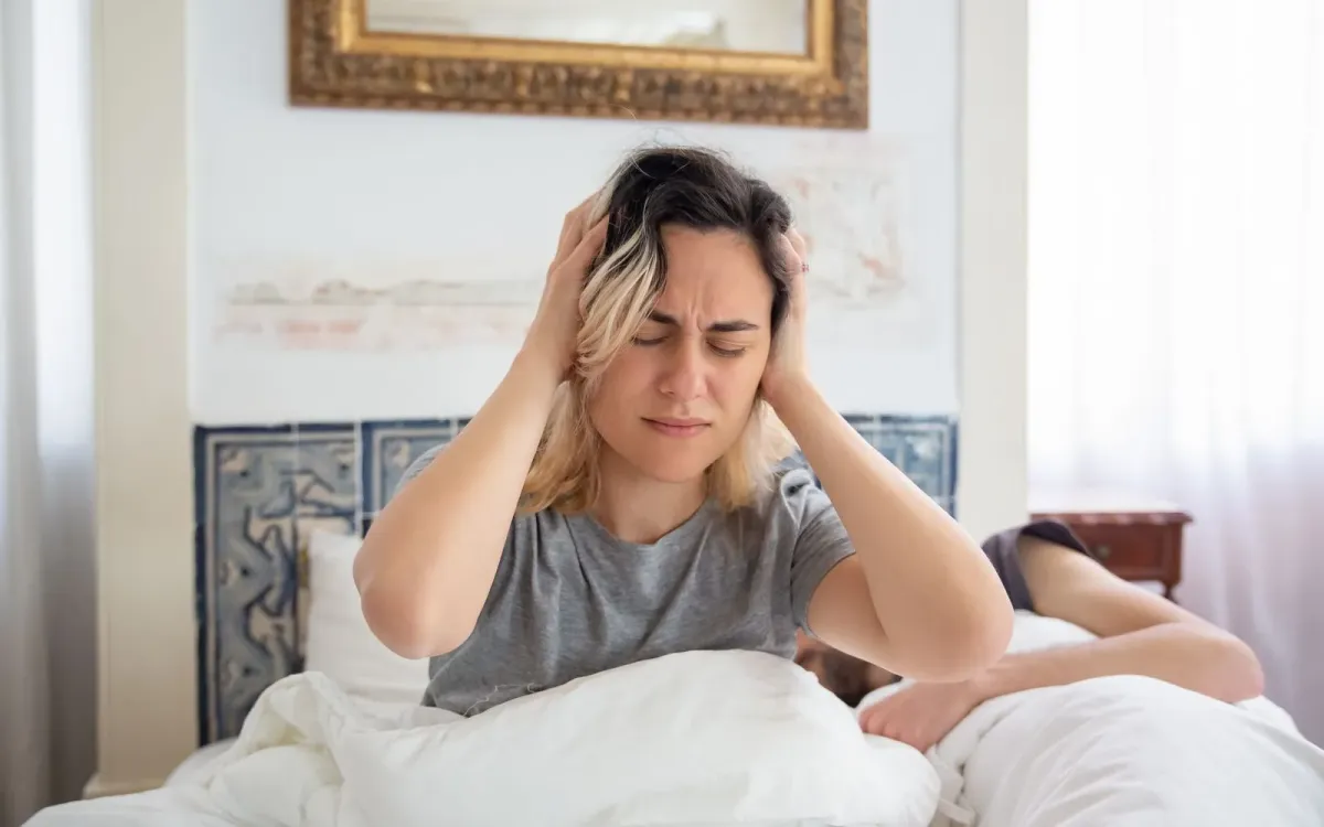Femme assise dans son lit, la tête entre les mains