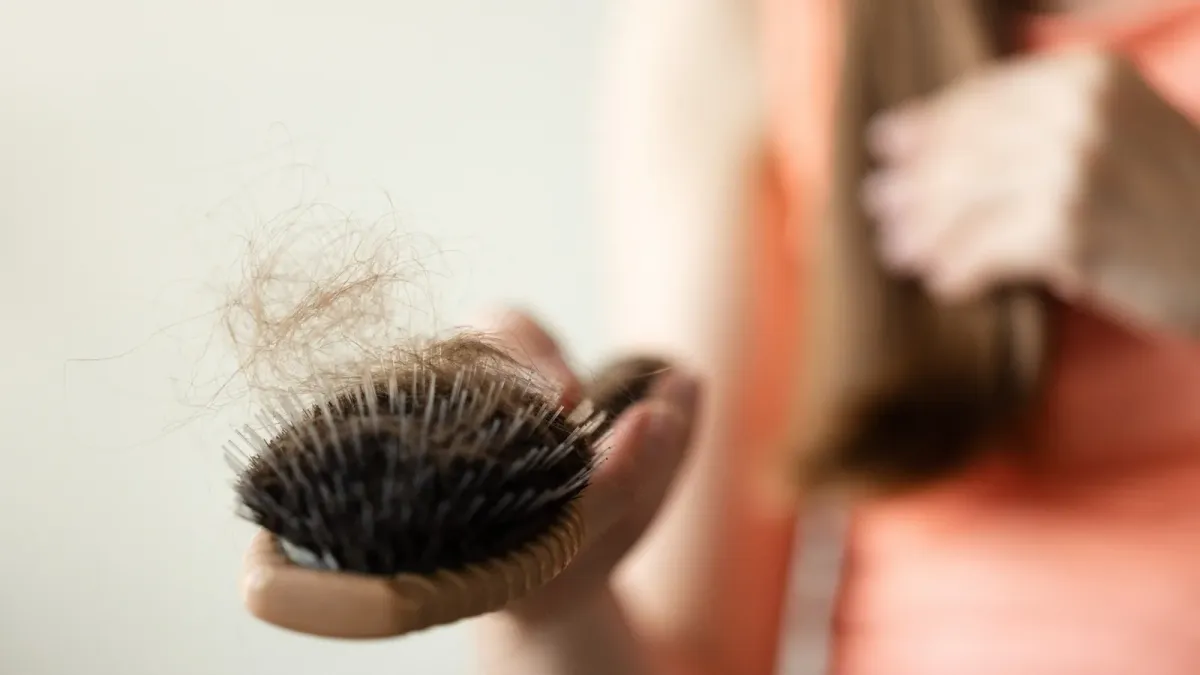 Brosse à cheveux tenue à la main, garnie de cheveux tombés