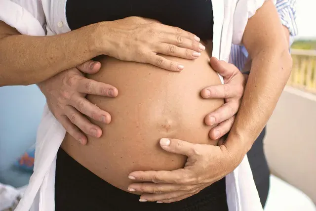 Deux paires de mains posées sur un ventre rond de femme enceinte
