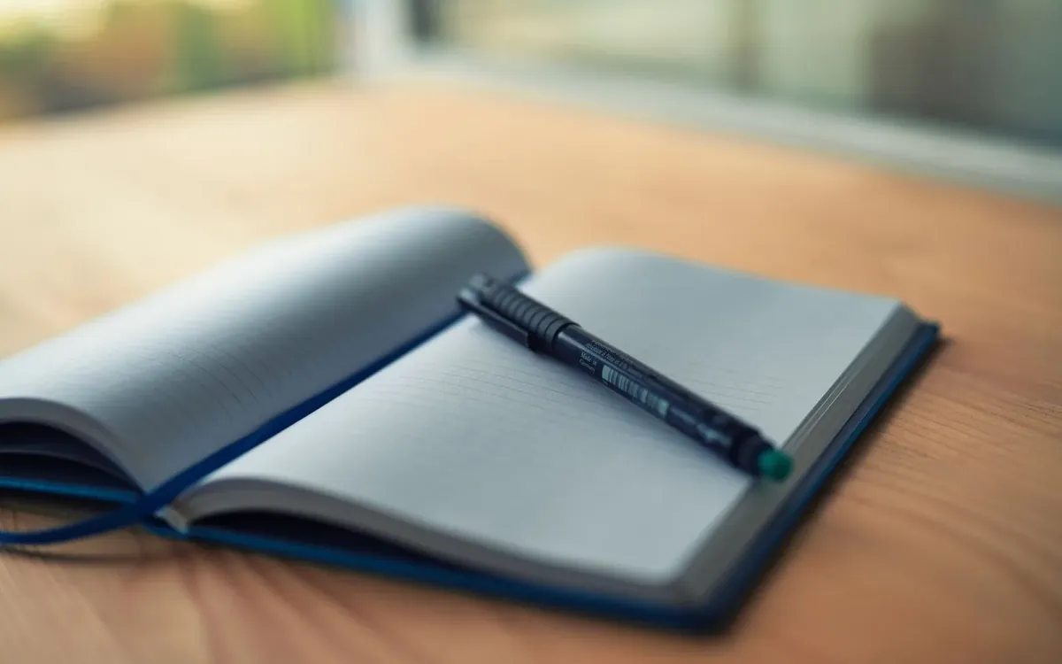 Carnet ouvert avec un stylo posé dessus, sur un bureau en bois