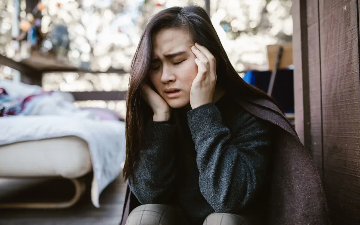 Femme assise au pied de son lit, la tête dans les mains, la nuit