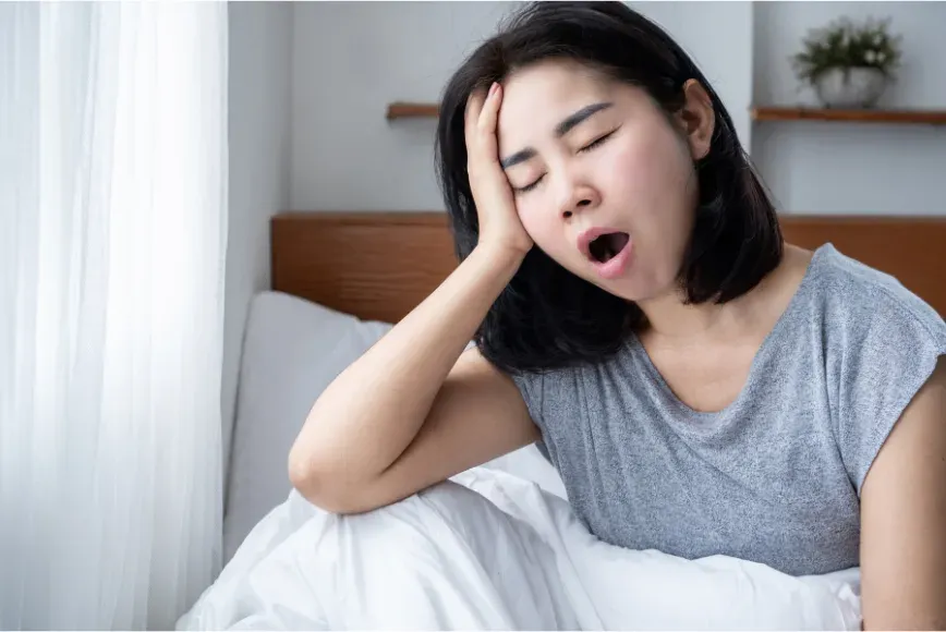 Femme assise dans son lit au réveil, la main sur le visage, en train de bâiller