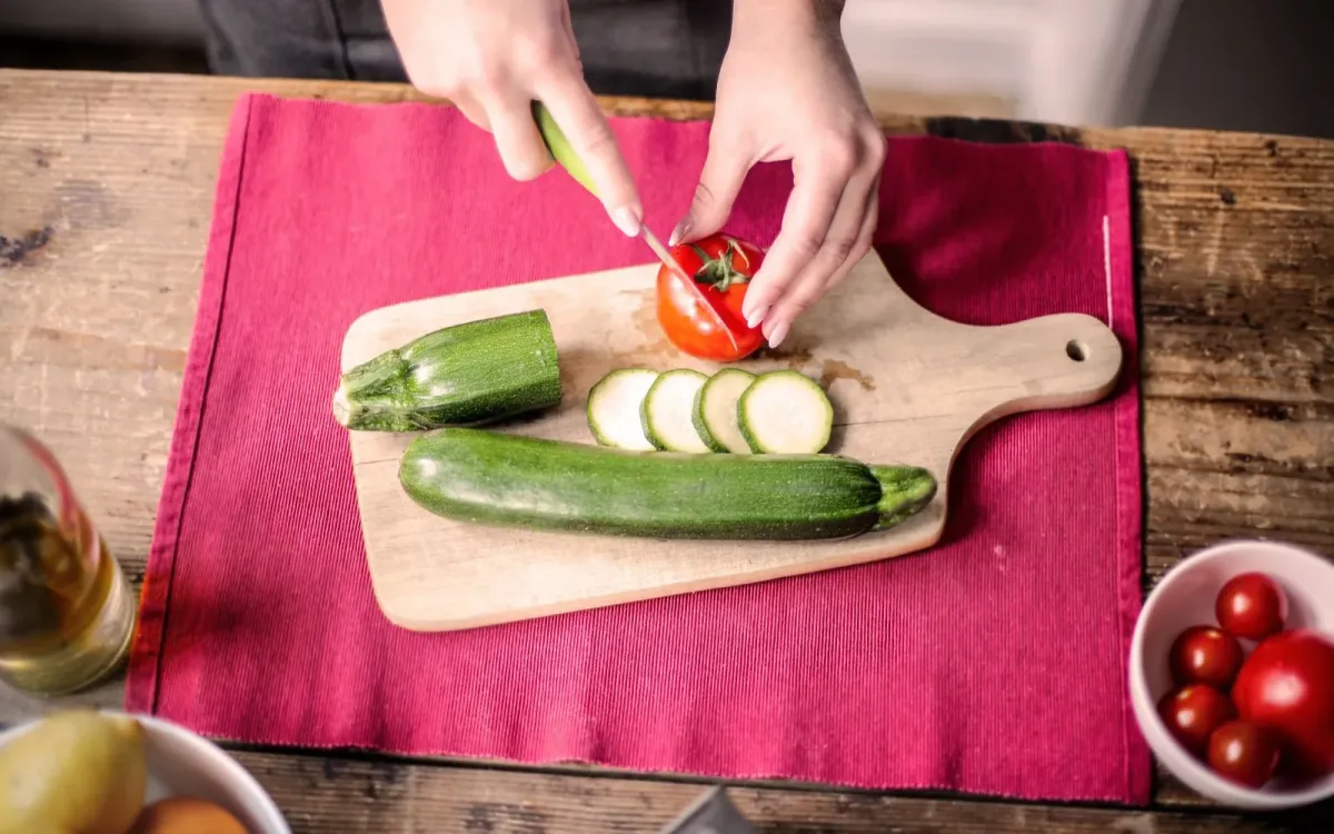 Mains qui découpent tomate et courgette sur une planche