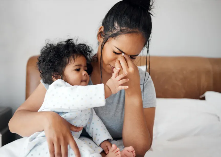 Jeune maman fatiguée tenant son bébé, la main sur le visage