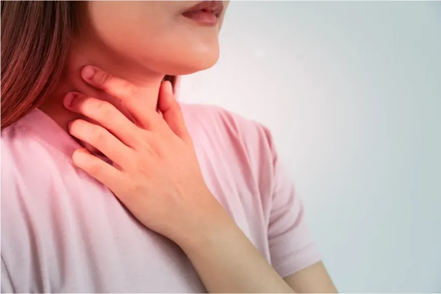 Femme qui pose la main sur le bas de son cou, à l'emplacement de la thyroïde