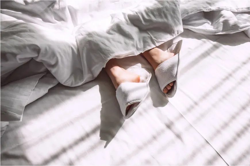 Jambes d'une femme sur un lit, dans la lumière filtrée des stores